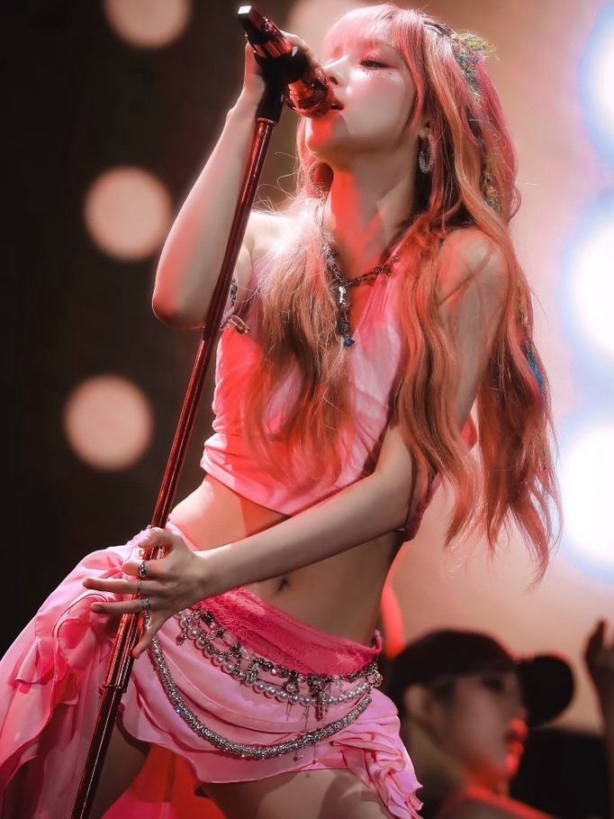 a woman with long red hair wearing a pink outfit and holding a microphone in her hand