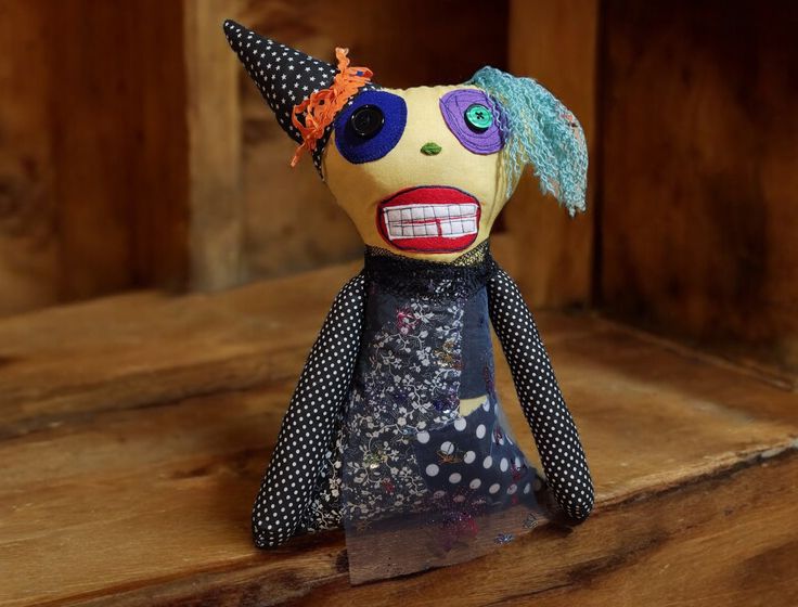 a cloth doll with blue hair and polka dots on it's face is sitting on a wooden shelf