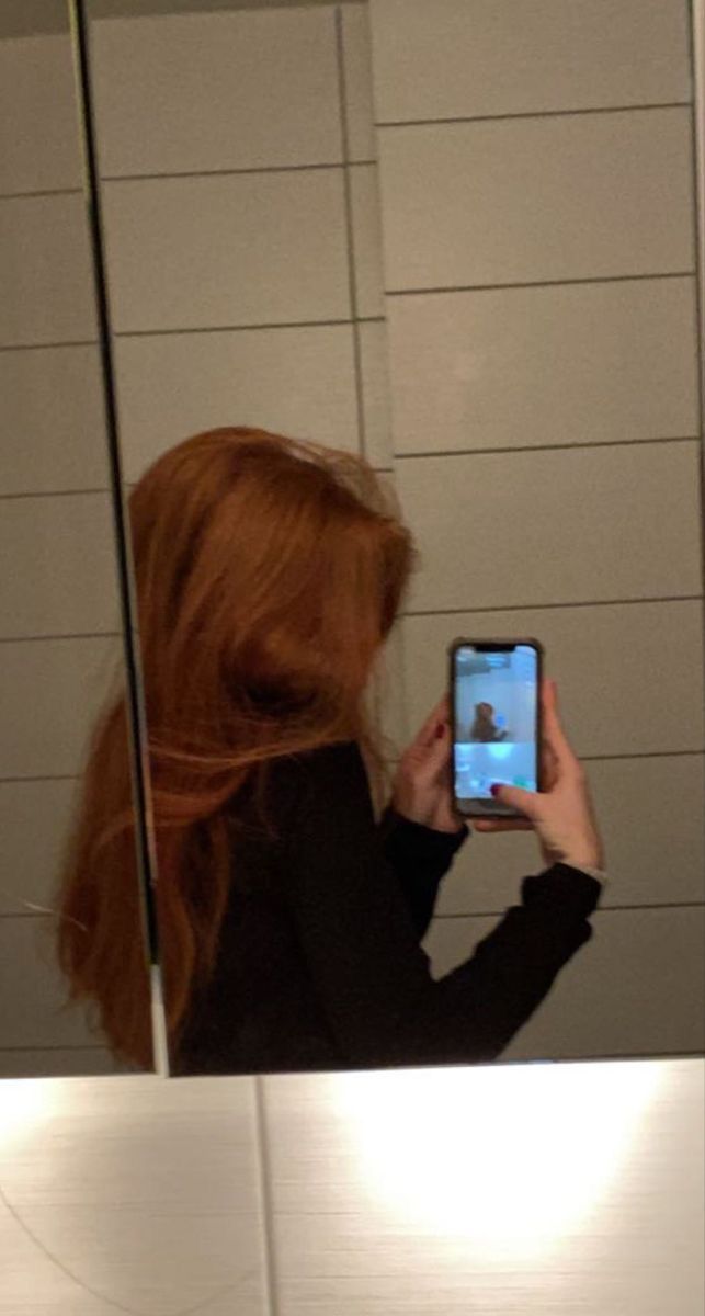 a woman taking a selfie in front of a bathroom mirror with her cell phone