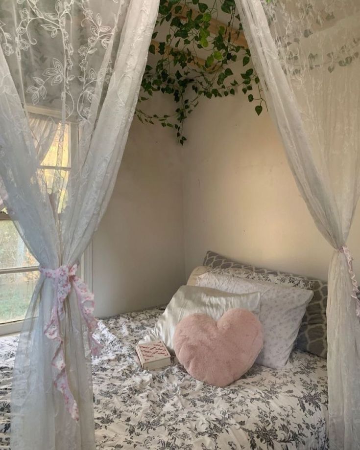 a bed with white curtains and pink heart shaped pillow on it's headboard