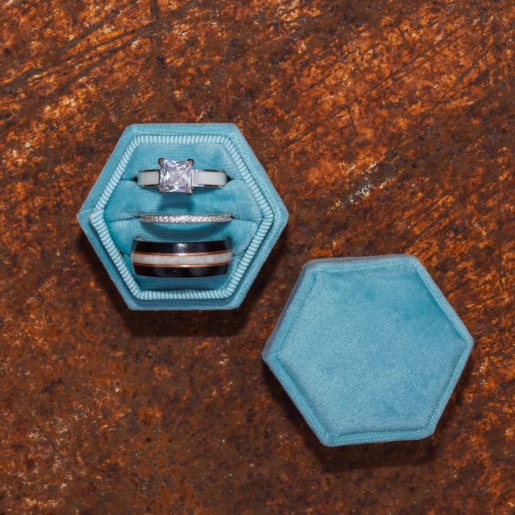 two wedding rings in a ring box on top of a brown marble table with a blue velvet case