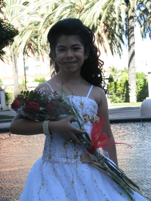 a girl in a wedding dress holding flowers and smiling at the camera with palm trees behind her