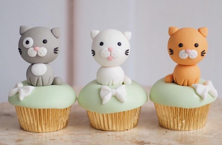 three cupcakes with cats sitting on top of them