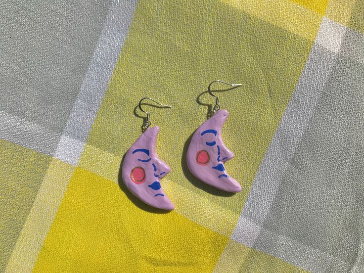 two pink and blue earrings sitting on top of a checkered tablecloth covered surface