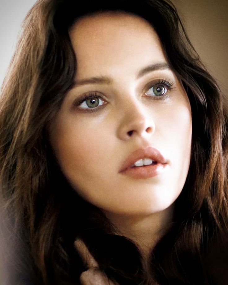 a woman with long brown hair and blue eyes is posing for the camera while holding her hand on her neck