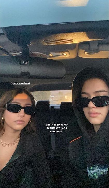 two women sitting in the back seat of a car wearing sunglasses and hoodie jackets