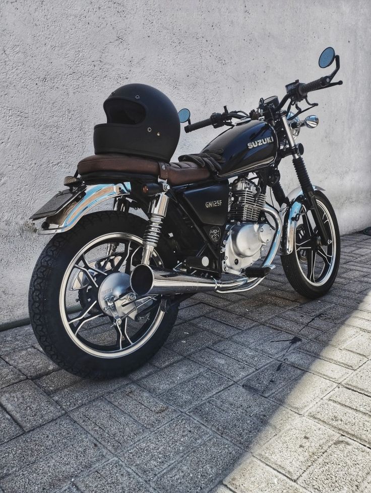 a black motorcycle parked next to a wall on a brick sidewalk with a helmet on the seat