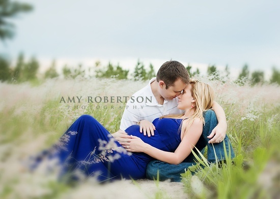 a pregnant couple cuddles in the tall grass