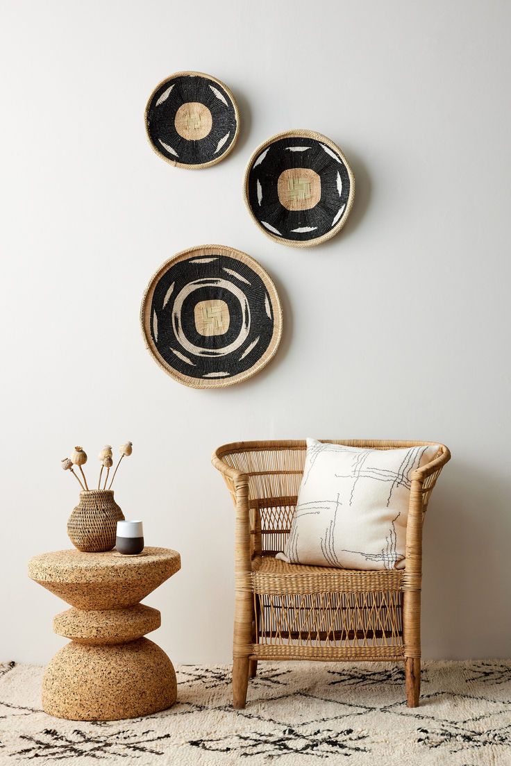 three black and white plates on the wall above a wicker chair with a vase