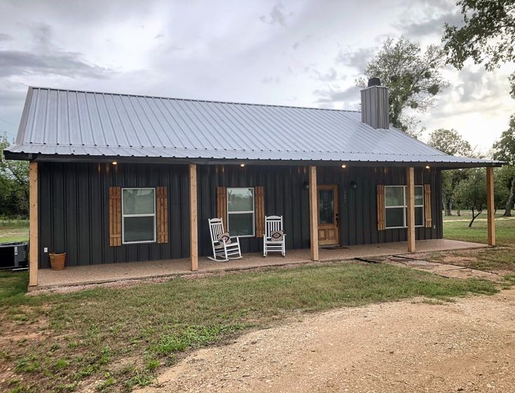 a black cabin with two chairs on the front porch and one door open to another room