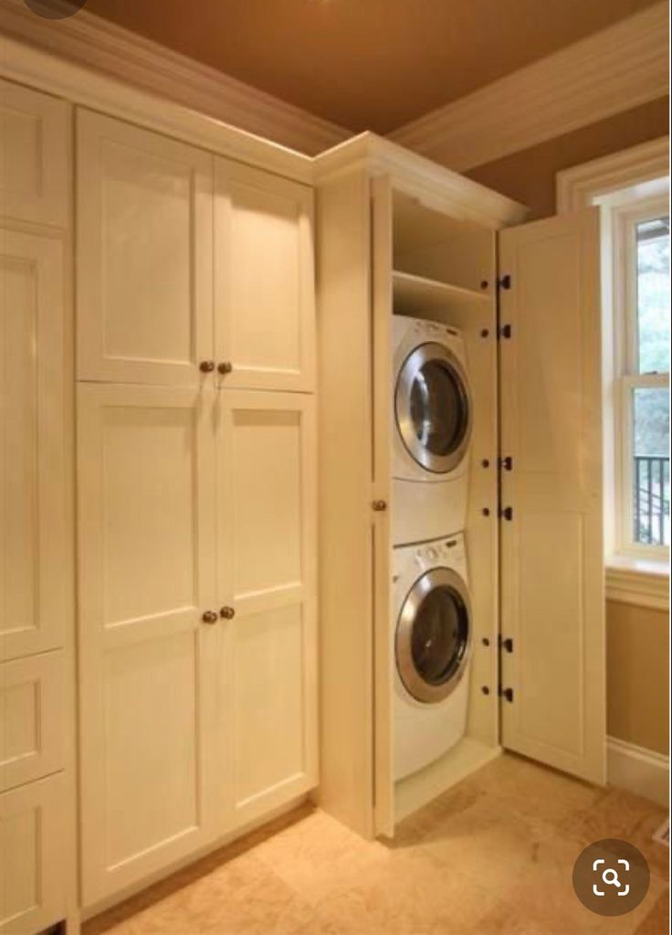 a washer and dryer are in the corner of a room with white cabinets