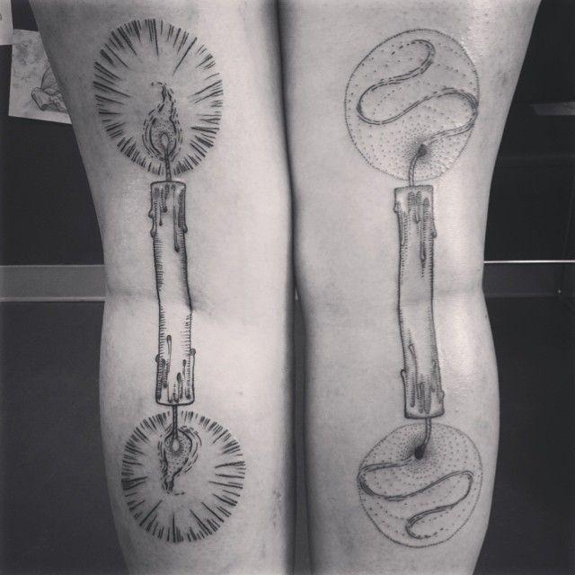 black and white photo of two legs with tattoos on them, one is holding a candle