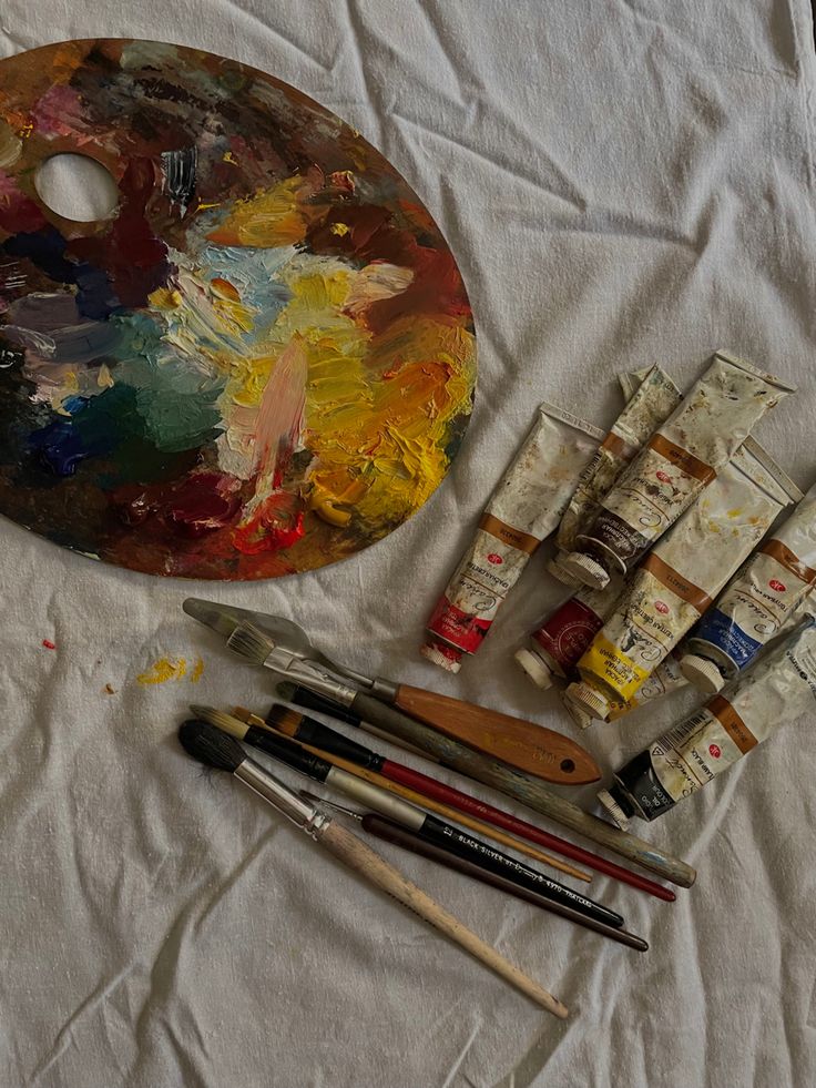 an artist's palette, paint and brushes on a white sheet