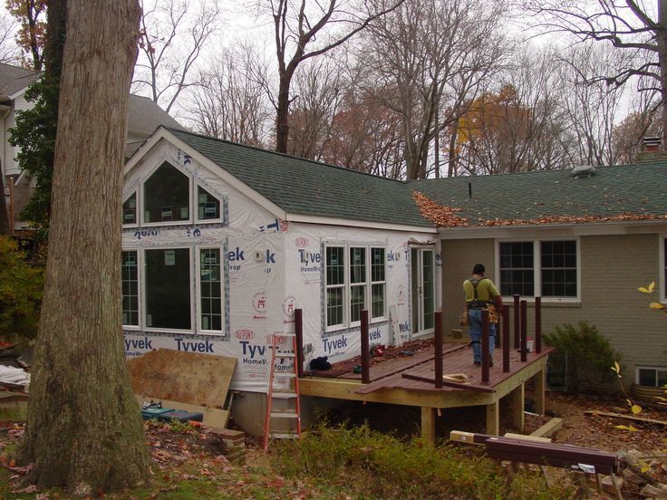 a man standing on the porch of a house under construction in front of a tree