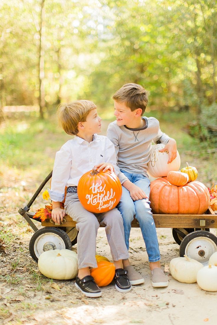 two boys sitting on a wagon with pumpkins