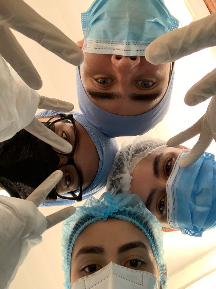 four doctors standing in a circle wearing masks and gowns on their heads, looking up at the camera