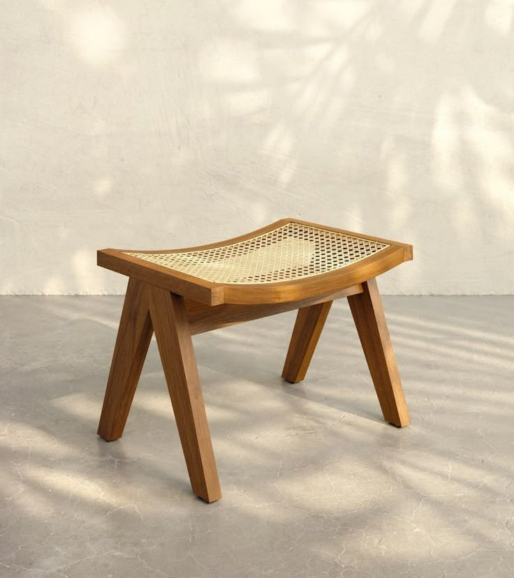 a small wooden bench sitting on top of a cement floor next to a white wall