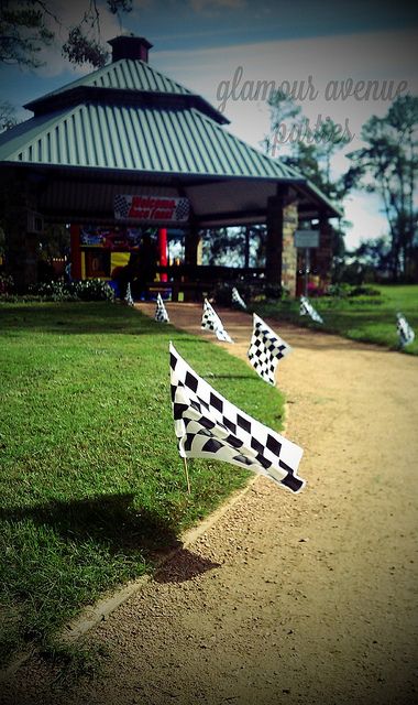 some flags that are in the grass near a building with a checkerboard flag on it