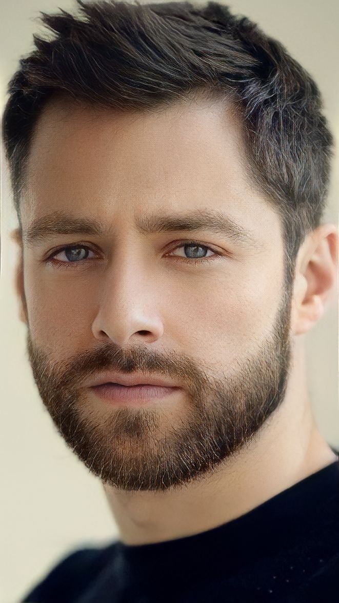 a close up of a man with a beard wearing a black shirt and looking at the camera