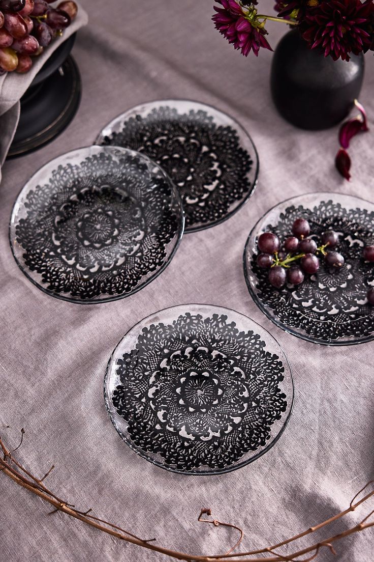 three black and white plates sitting on top of a table covered in grapes next to a vase