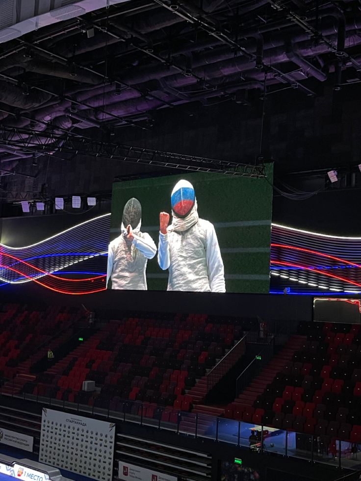 two men standing in front of a large screen on the side of a basketball court