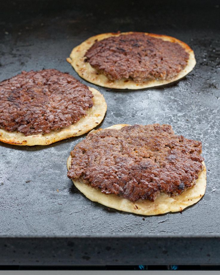 three hamburger patties sitting on top of a baking sheet