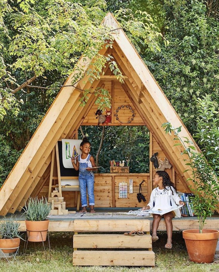 two children are standing on the roof of a small house made out of wooden planks