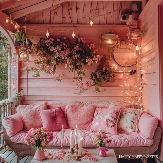 a pink couch sitting on top of a wooden porch next to a table filled with flowers