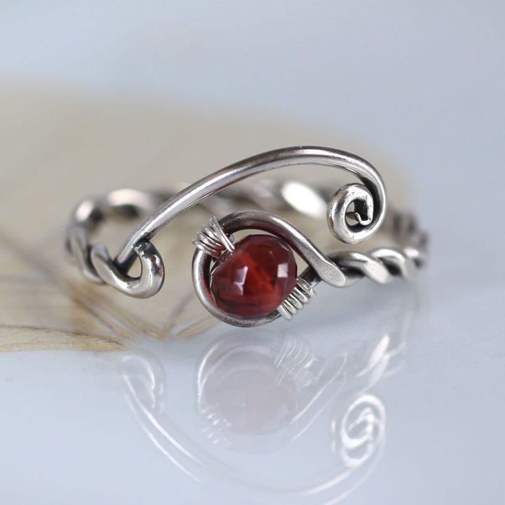 A special silver and garnet ring with a twist and open spiral design. It's adjustable and perfect as a gift if you're not quite sure of the size you need. The shank is twisted from one wire and in the loop at the end is nestled an AA-plus faceted wine red garnet bead and the opposite ends are shaped into spirals. Both twists and spirals are classic and has been used since Celtic times in jewellery. I think my Danish heritage is shining through. :o) Garnet is a stone of positive thoughts which is Pretty Wire Ring, Wire Jewellery Rings, Silver Wire Wrapped Metal Rings, Devil Wire Ring, Red Vintage Wire Wrapped Jewelry, Wire Mushroom Ring, Katniss Ring Trollbeads, Goth Wire Rings, Gothic Wire Ring