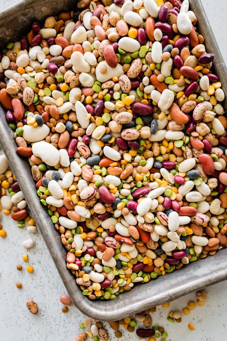 a metal pan filled with different colored beans and corn on top of a white surface