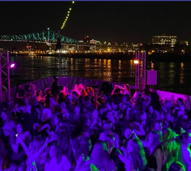 a large group of people dancing in front of the water with a bridge in the background