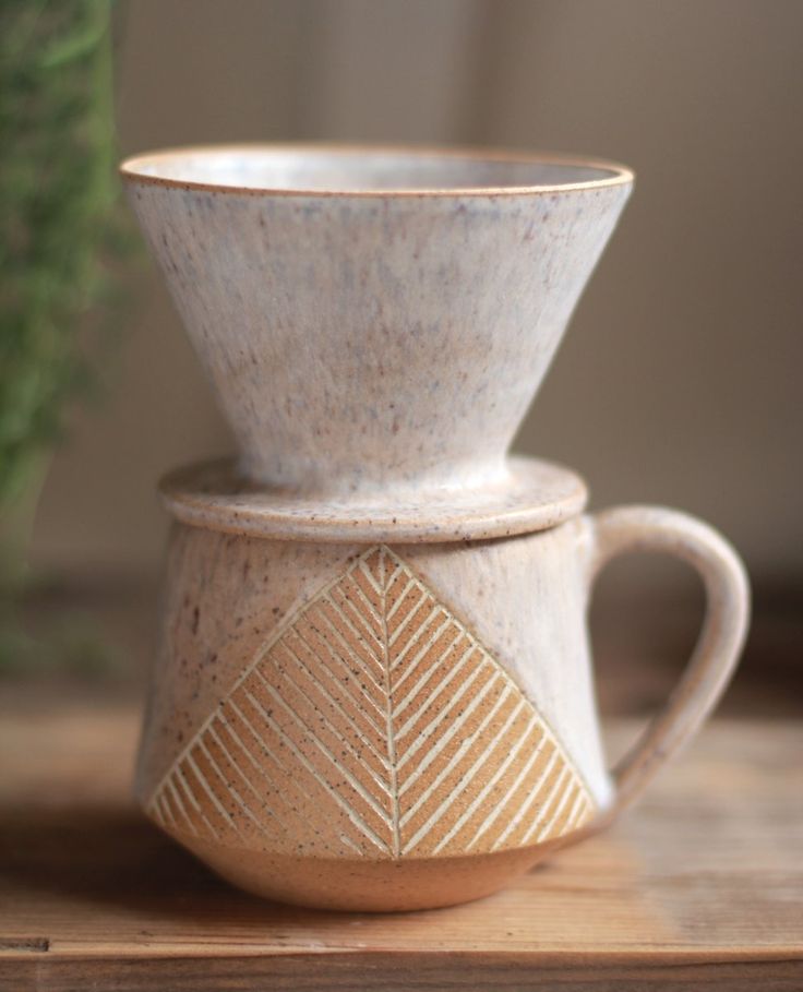 two cups sitting on top of a wooden table next to a potted green plant