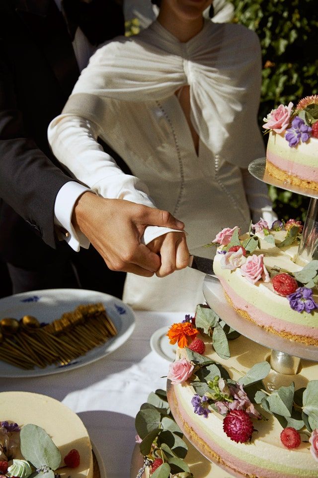 a bride and groom are cutting into their wedding cake at the table with flowers on it