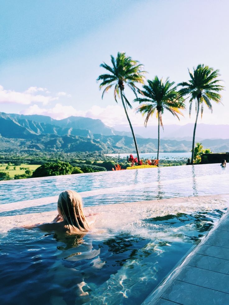 a woman is sitting in the middle of a swimming pool with palm trees behind her