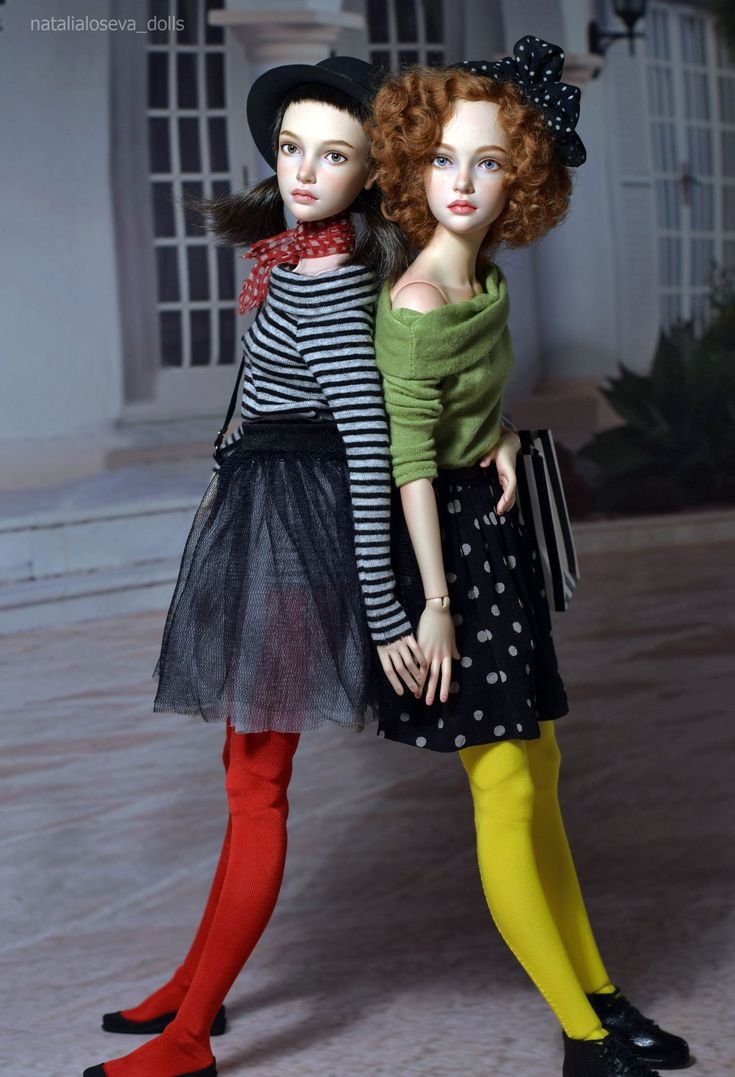 two dolls standing next to each other in front of a white building with red hair