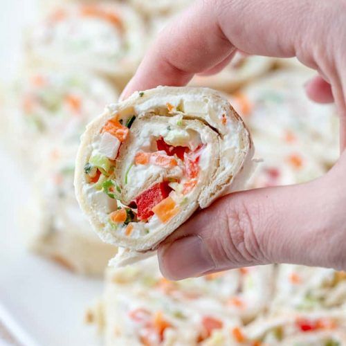 a hand holding a vegetable wrap over a white plate