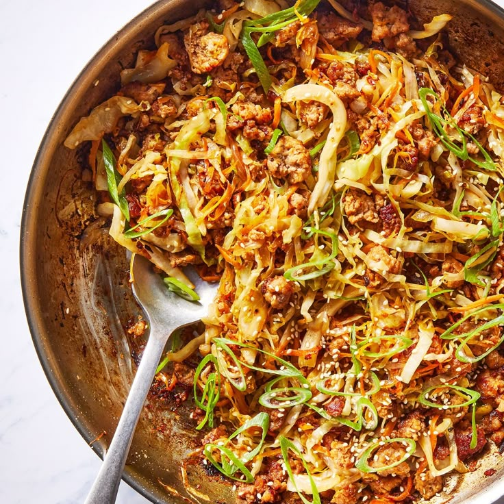 a pan filled with meat and vegetables on top of a white countertop next to a silver spoon