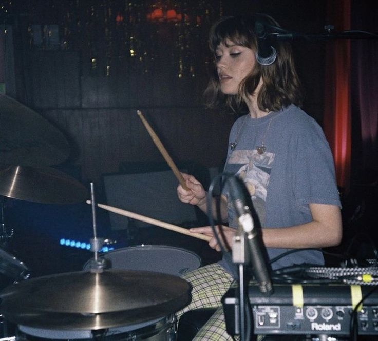 a woman sitting in front of a drum set with headphones on her ears, playing the drums