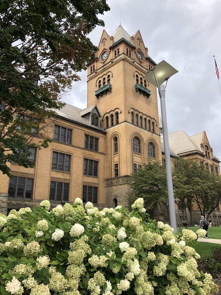 a tall building with a clock on the top of it's tower and flowers in front