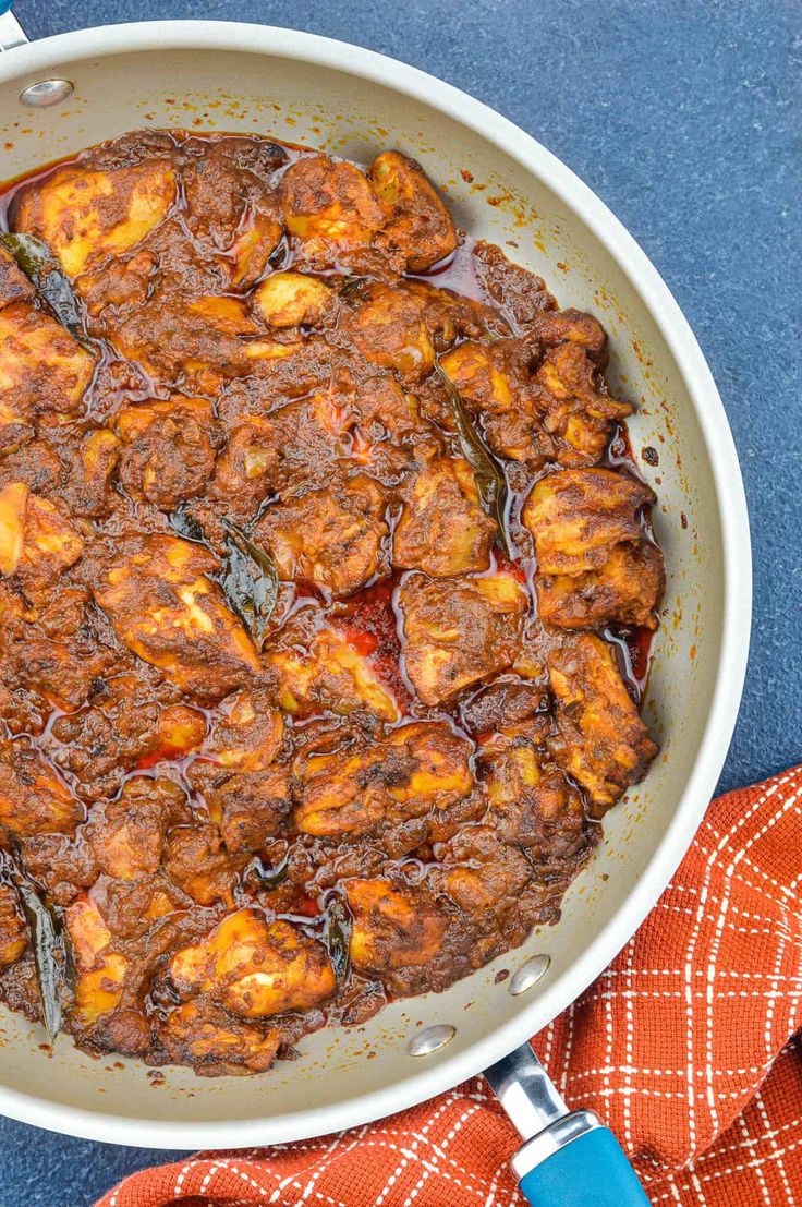 a pan filled with meat and sauce on top of a blue table cloth next to an orange towel