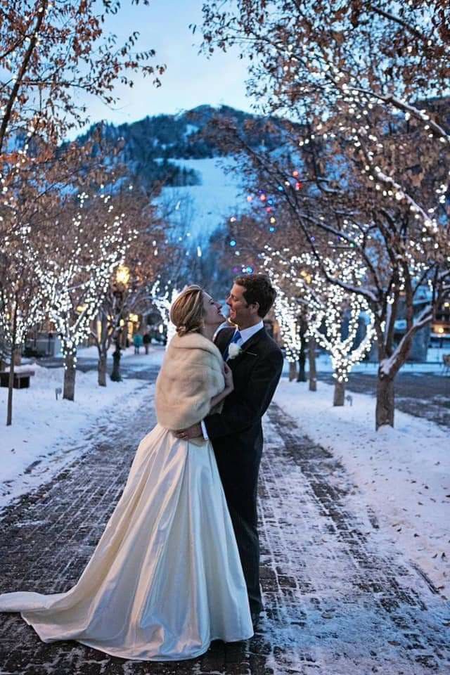 a bride and groom are standing in the snow under trees with their lights on them