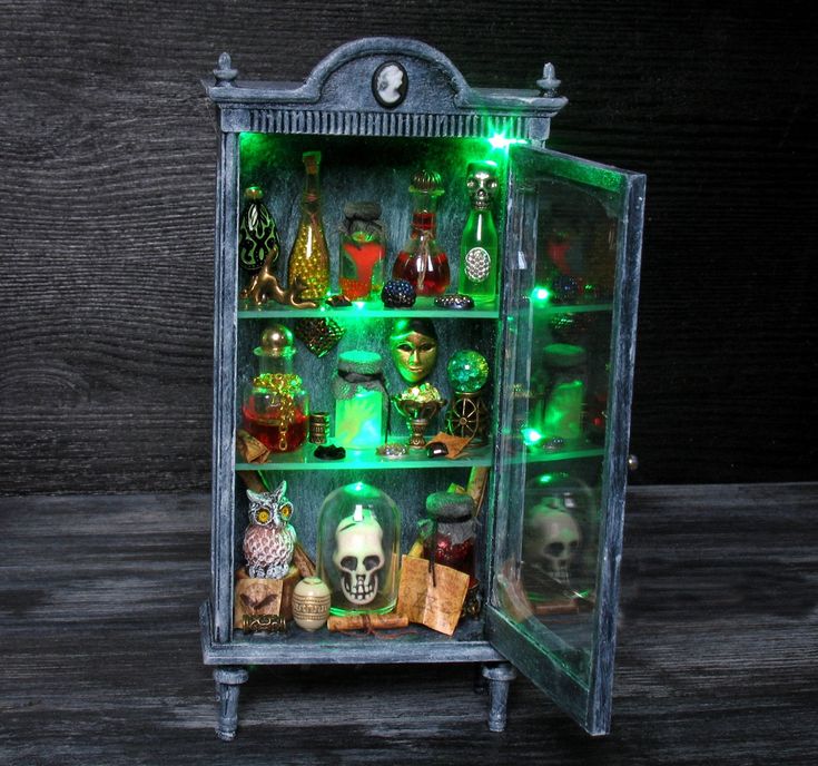 an illuminated display case filled with bottles and skull figurines on top of wooden flooring