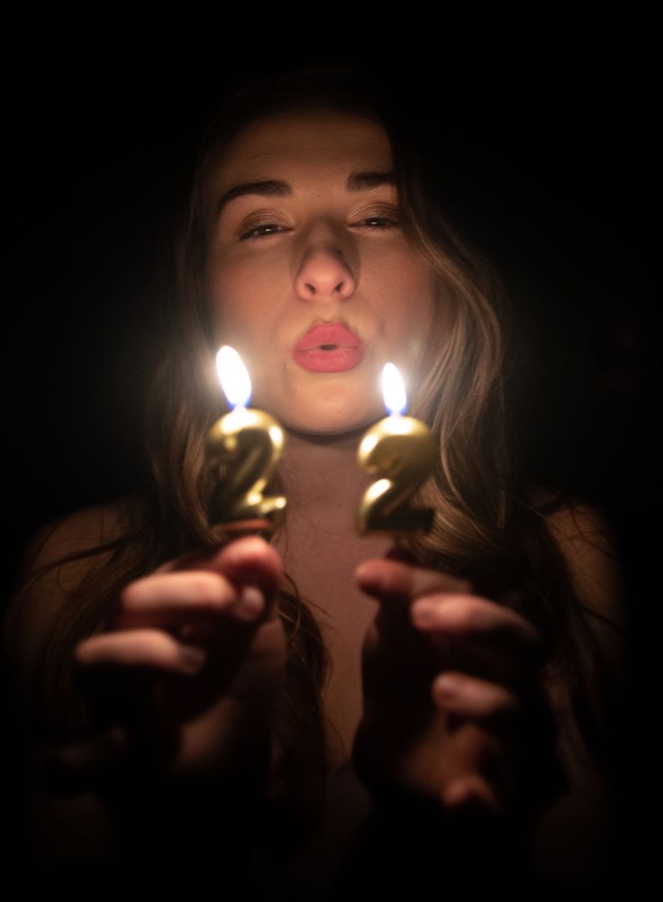 a woman holding two candles in front of her face with the light shining on her