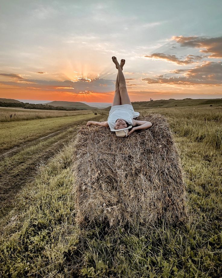 a person laying on top of a hay bale in the middle of a field