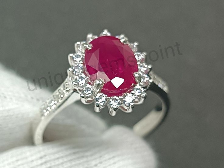 a close up view of a ring with a large red stone in the center and small white diamonds around it