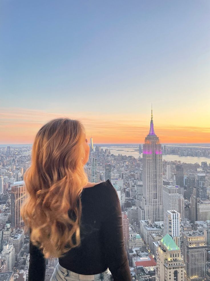 a woman standing on top of a tall building looking down at the cityscape