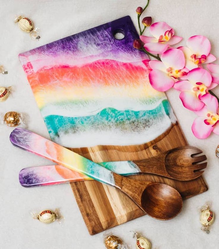 a wooden cutting board with utensils on it next to orchids and candy