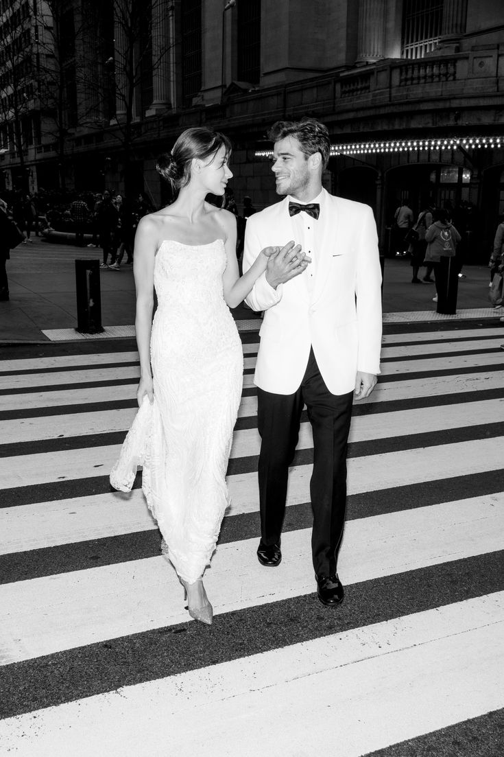 a man in a tuxedo and a woman in a dress are walking across the street