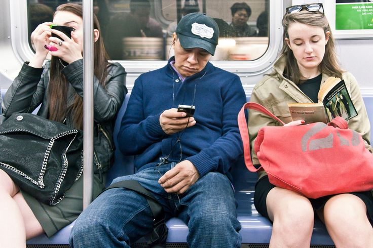 three people sitting on a subway looking at their cell phones and one person holding a purse