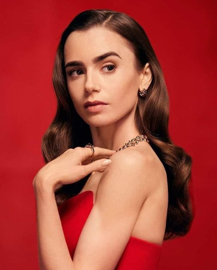 a woman in a red dress posing with her hand on her shoulder and wearing gold jewelry